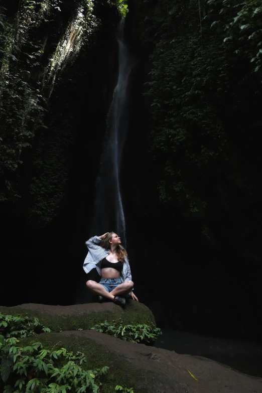 a woman in blue shirt standing in front of a waterfall