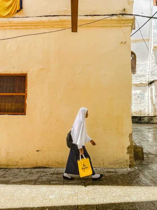 an old woman walking down the street in front of a tan building