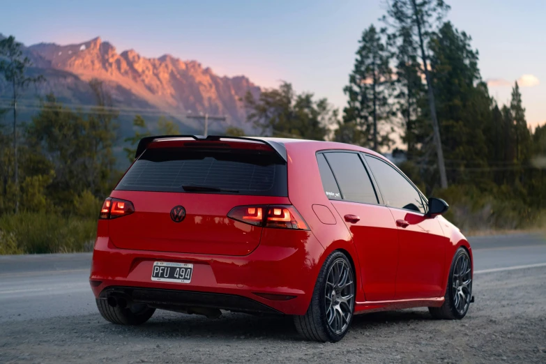 the back of a red car driving down a road with mountains in the background