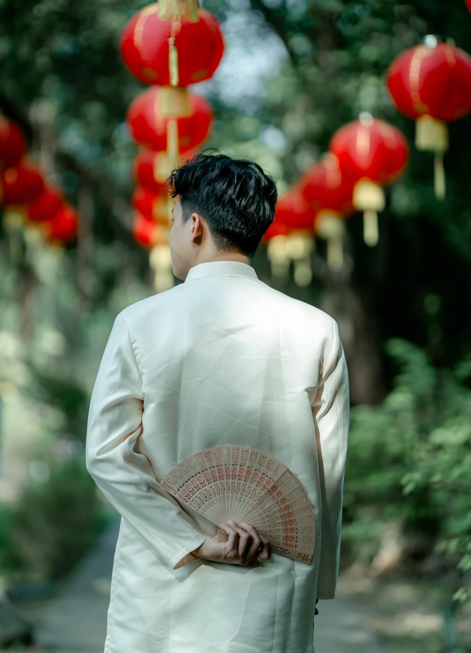 man dressed in traditional clothing standing near the sidewalk and holding an asian fan