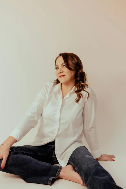 a woman sitting on a white floor wearing jeans and a white shirt