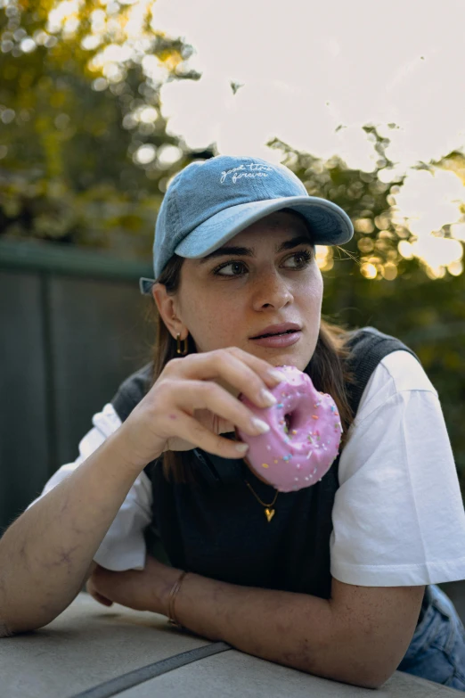 a woman wearing a hat sitting on a bench with a donut