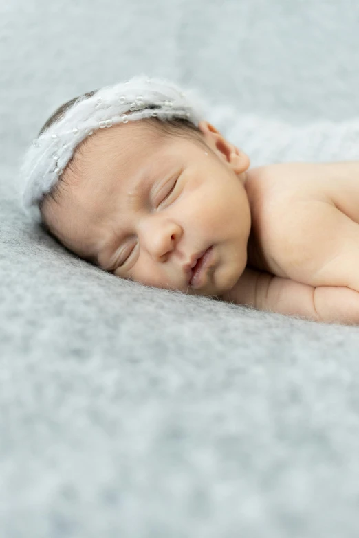 a baby girl with a headband sleeps on a grey blanket