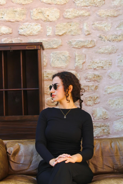 a young woman in black sitting on a brown couch