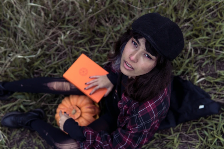 a girl in a hat and black boots holds an orange book