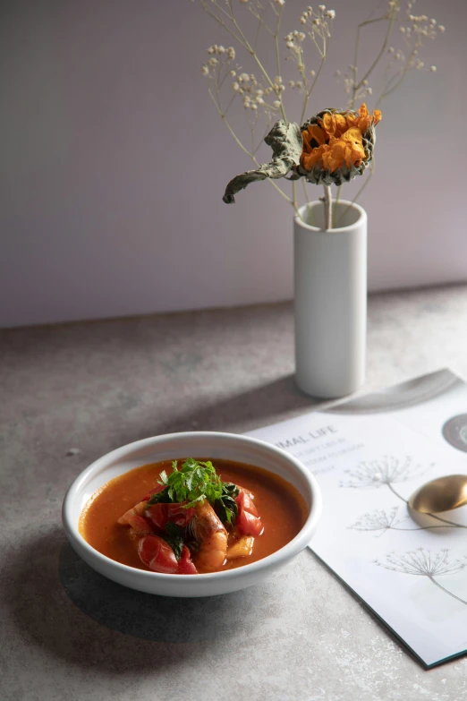 a bowl of red soup with spinach and meat on a table with a spoon