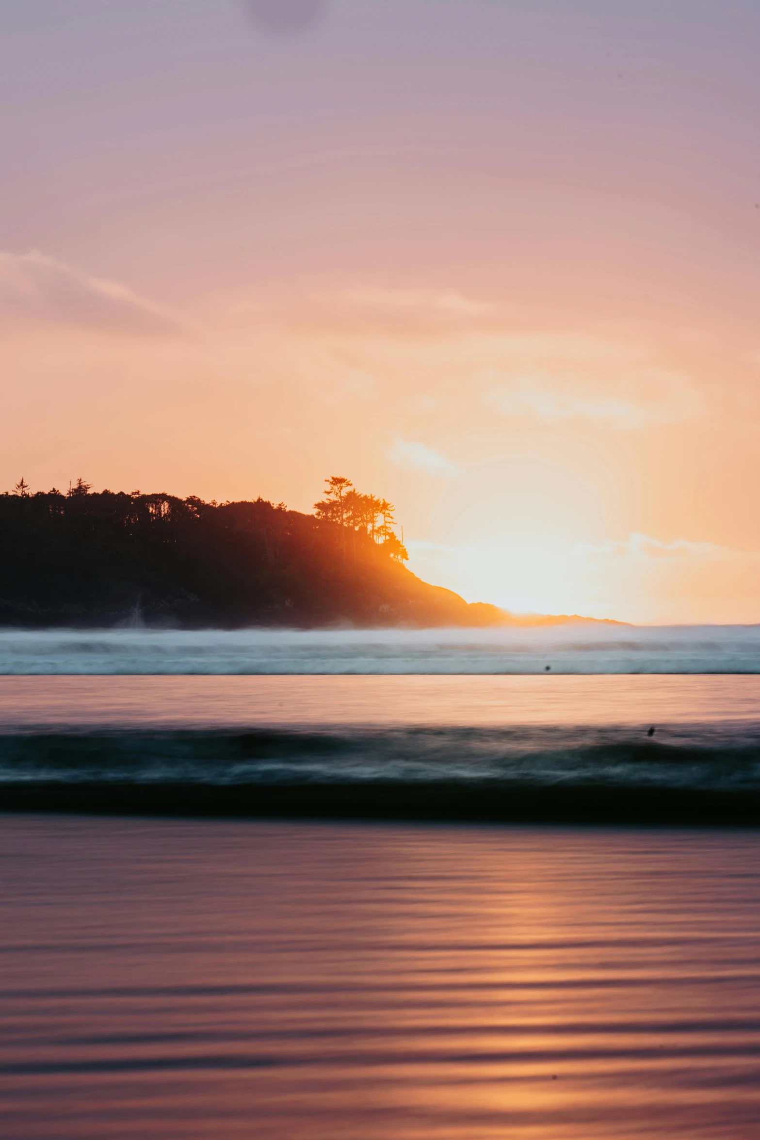 a surfer looks out at a sunset on the ocean