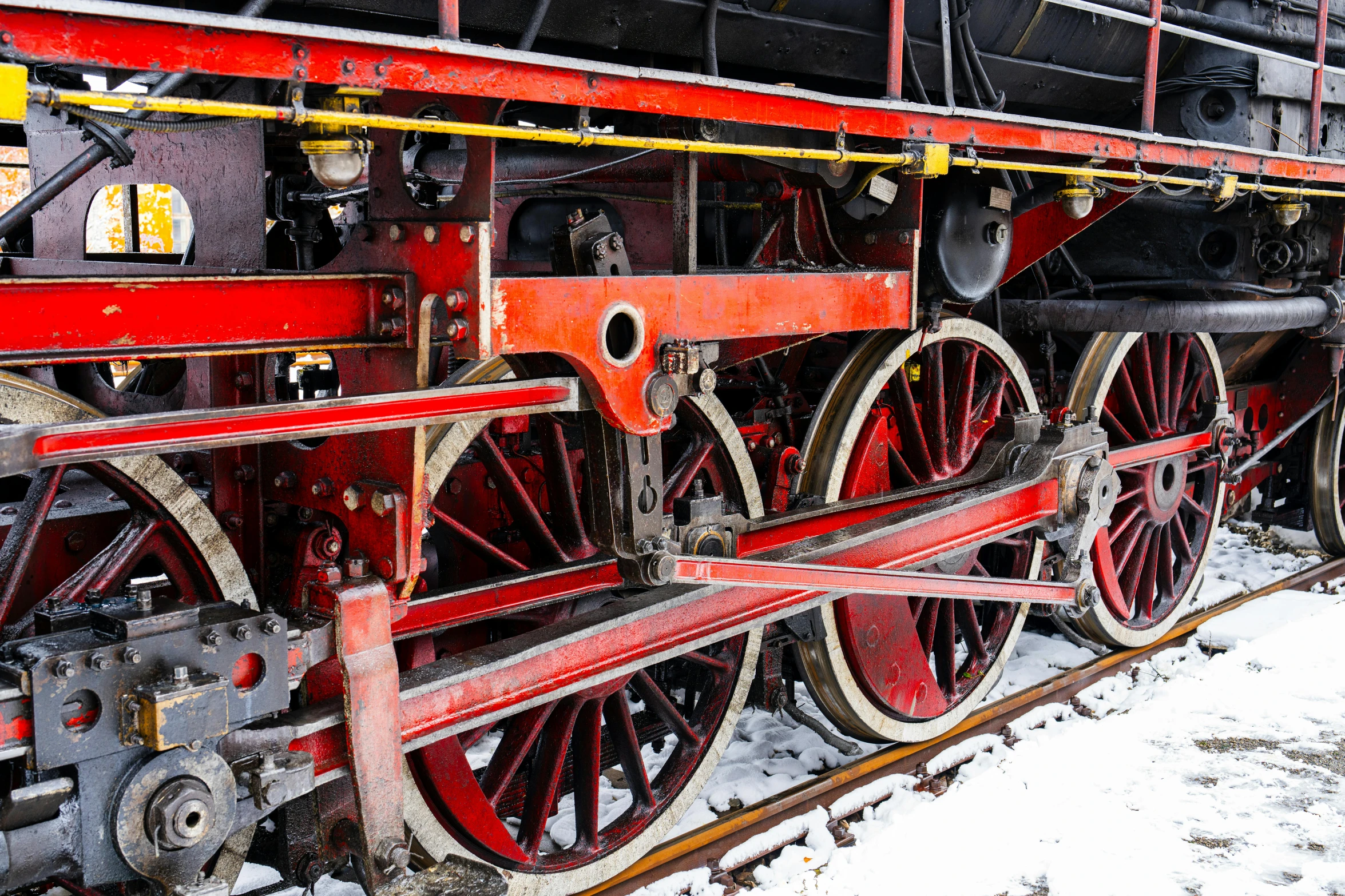 the wheels of an old red passenger train sit on snow covered tracks