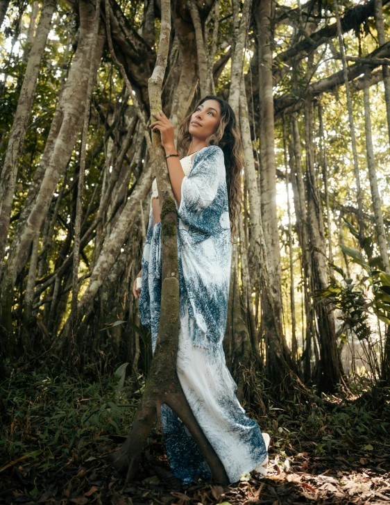 a beautiful woman in blue dress leaning on a tree