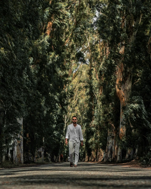 a man walks on the middle of the street in between tall trees