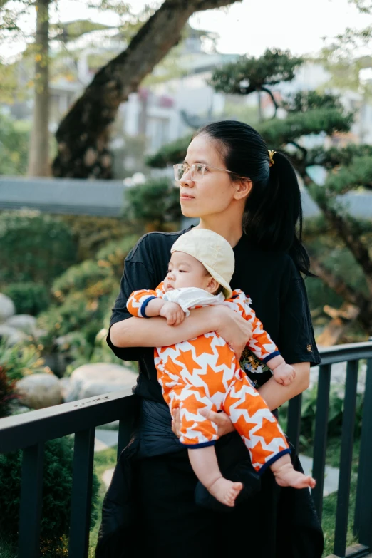 a woman holding a child on a railing near a tree