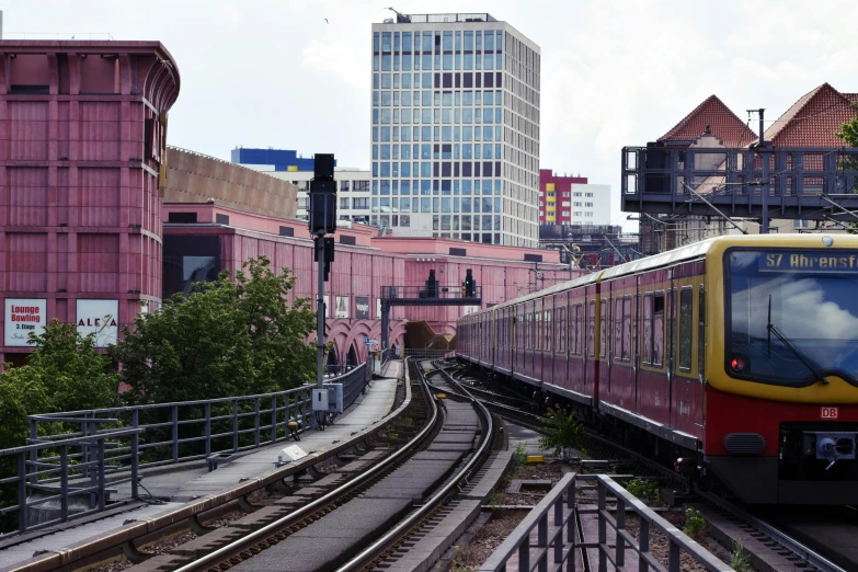 a red and yellow train traveling down tracks near tall buildings