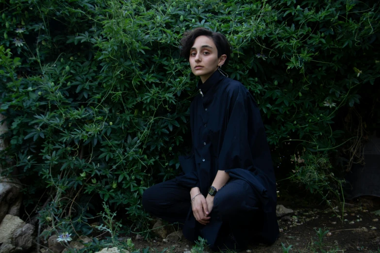 a woman kneeling down in the grass by some bushes