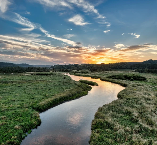 a river meandering down the middle of a grassy field at sunset