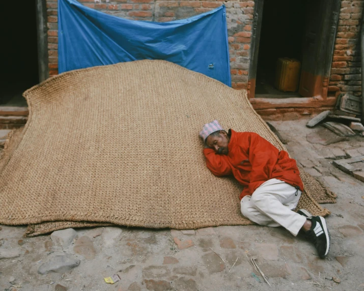 a man sitting on a brown blanket next to two blue tarp