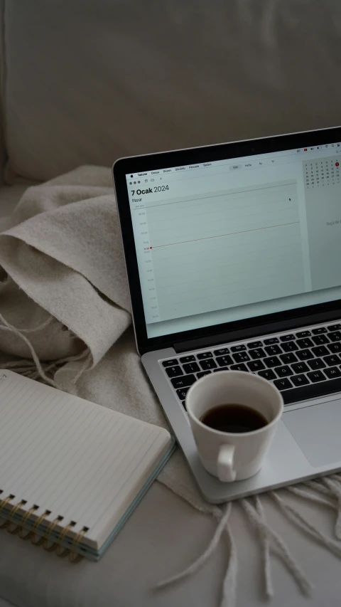 a laptop computer sits next to a cup of coffee on a bed