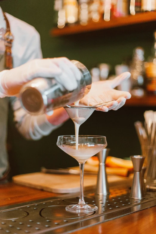 someone pouring martini into a glass at the bar