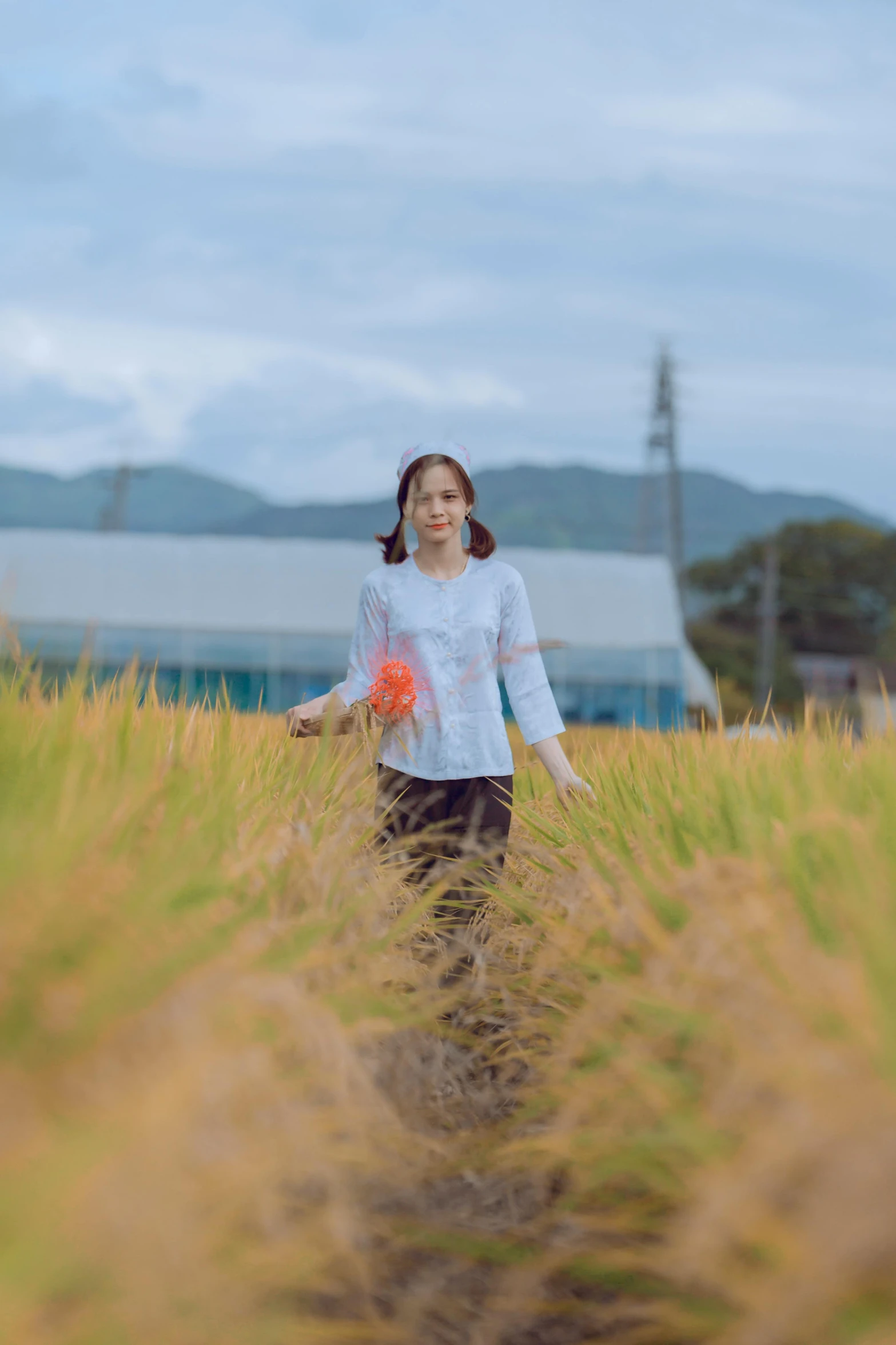 a young woman walking through tall grass holding a flower