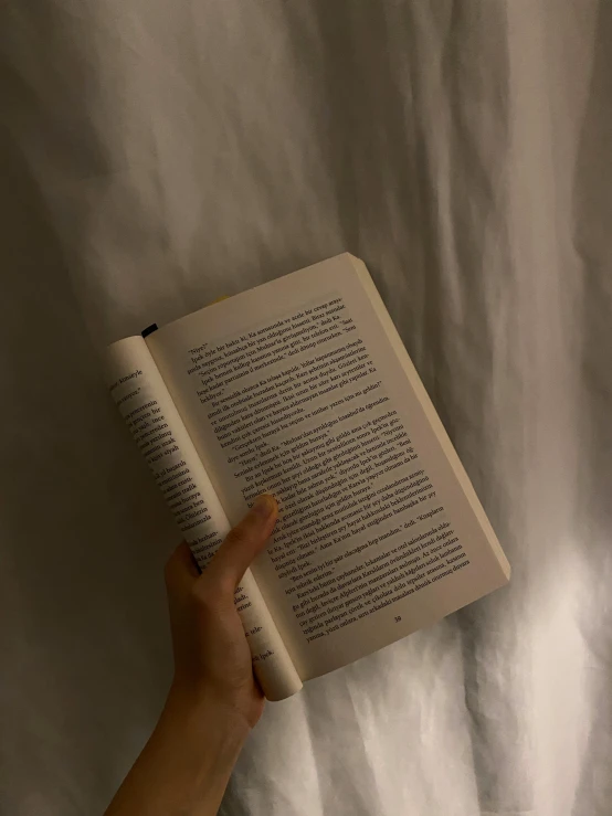 a hand holding an open book on top of a bed