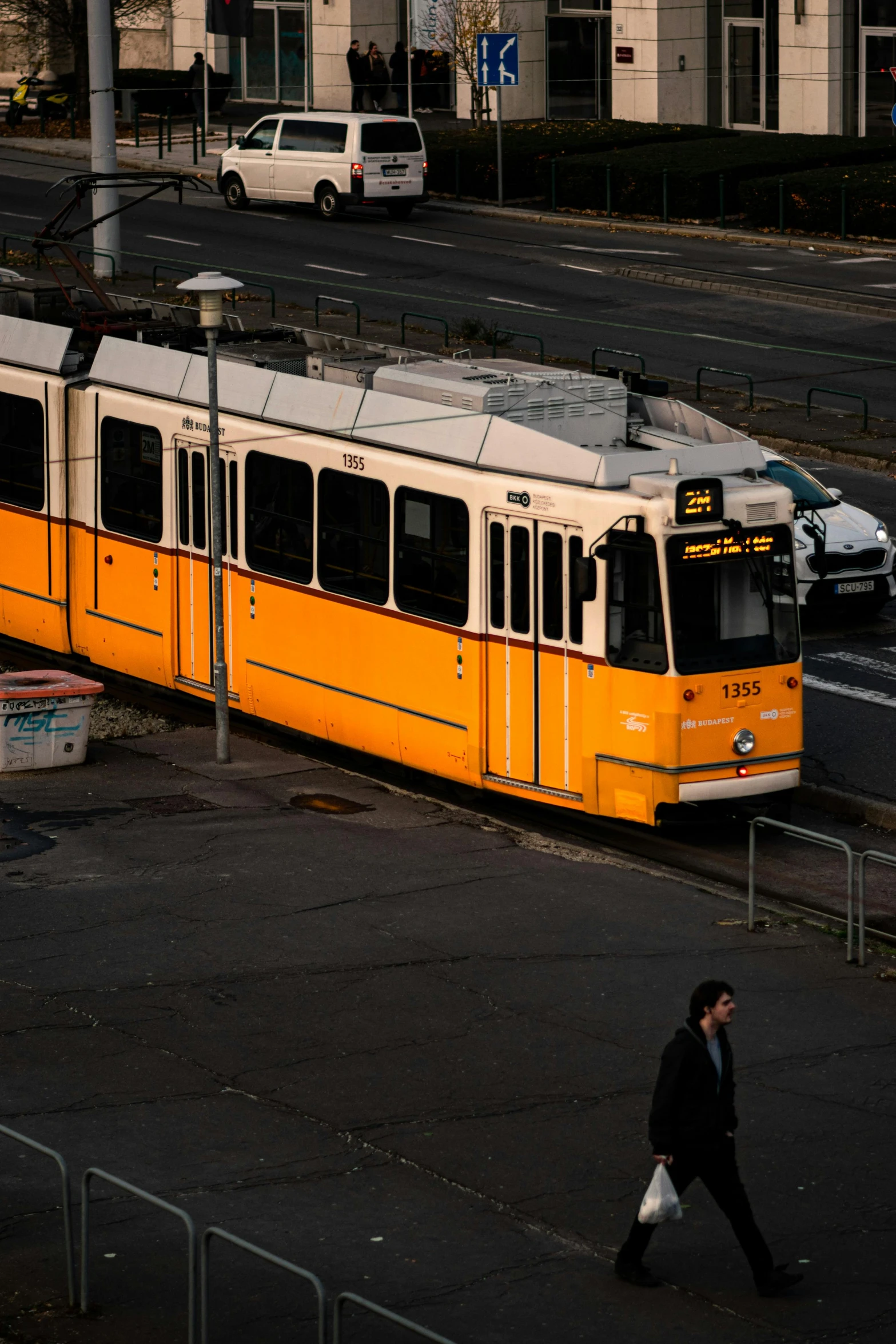 a man walks across the road past a tram