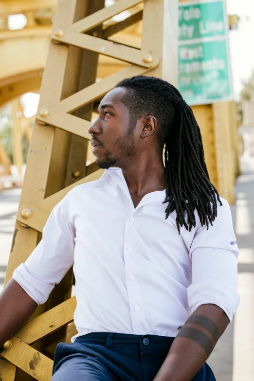 an african american man with long hair and white shirt leaning against a wooden structure