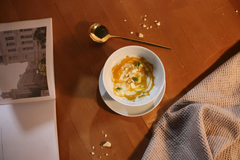 a small white bowl of food next to a spoon and magazine