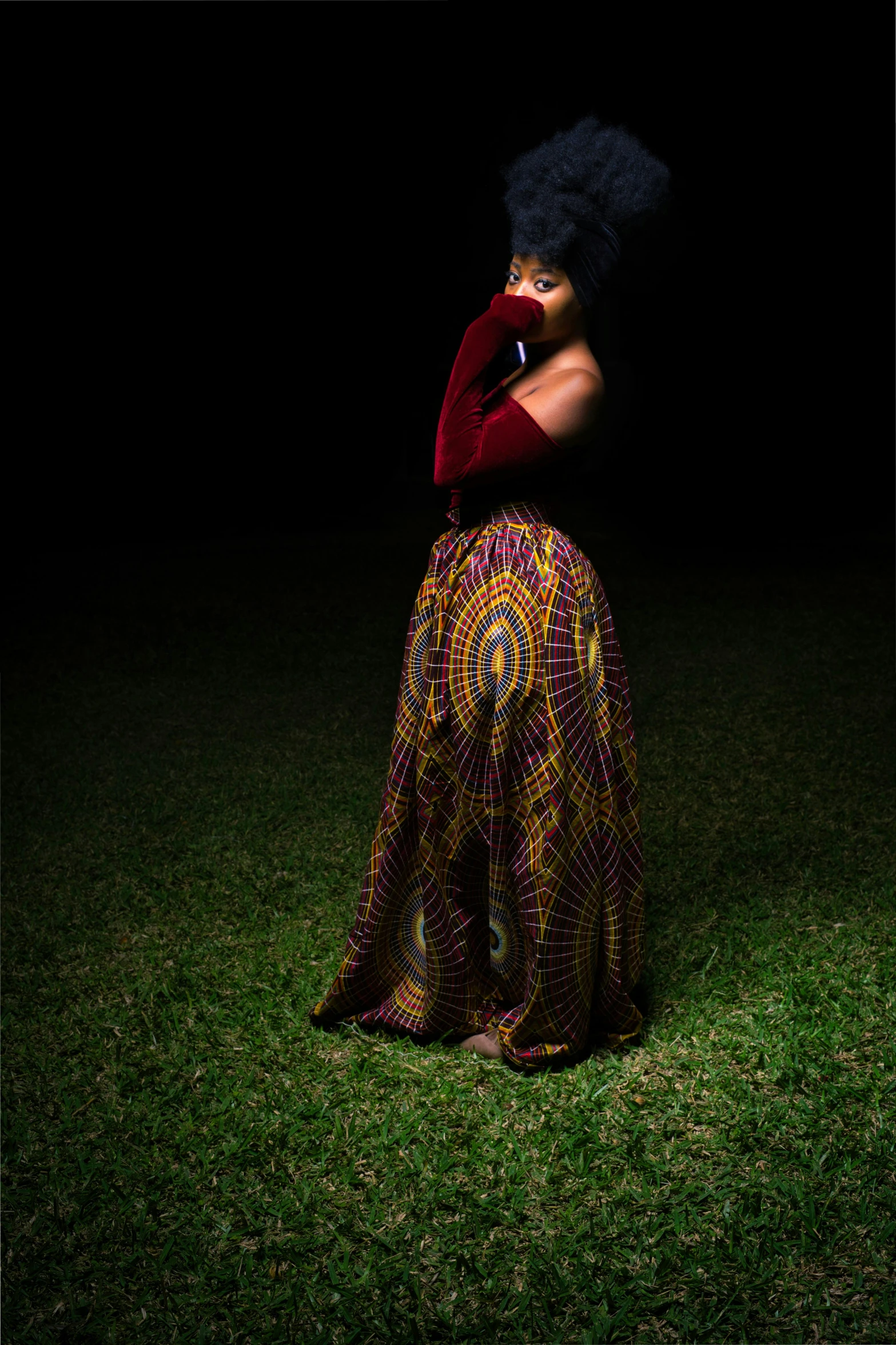 woman with a black afro, a red sweater, a colorful skirt and a black feather headpiece