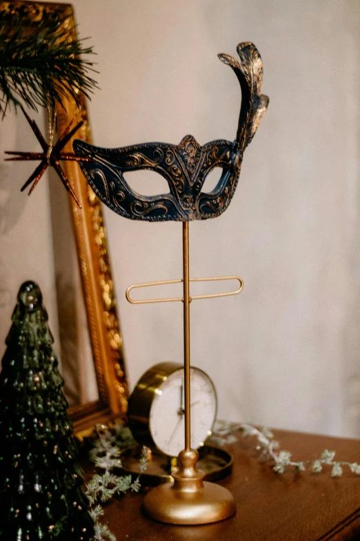 a mask is on a clock and sits next to christmas tree