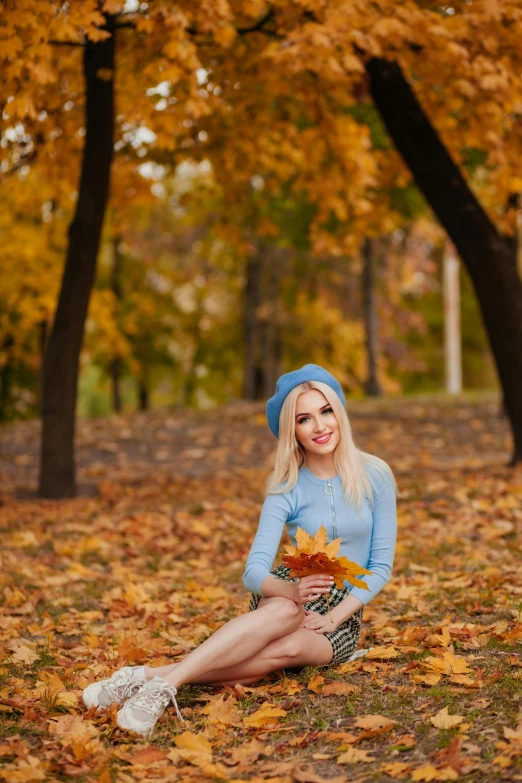 a beautiful blond sitting on the ground holding autumn leaves