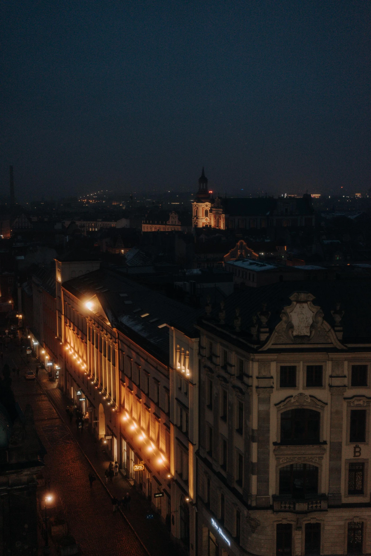 a night time view of a building with its lights on and cars driving down the street