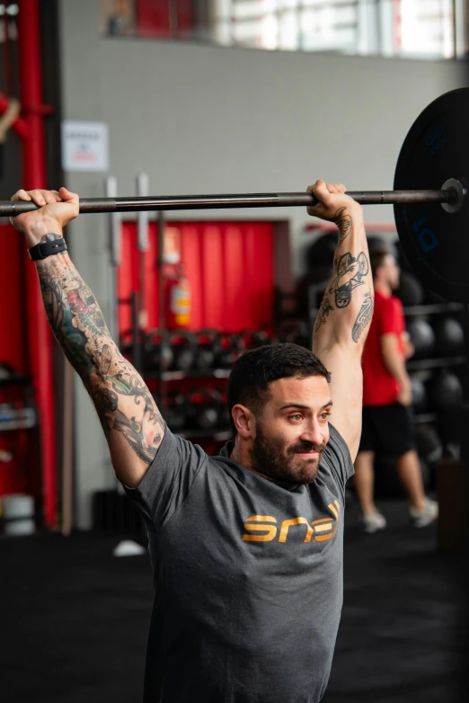 a man is holding up a barbell while the other one looks on