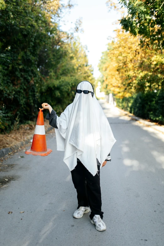 the man is dressed like an nun and he is holding a traffic cone