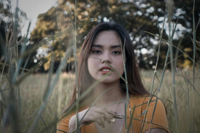 a young woman holds a small plant and stares at the camera through the tall grass