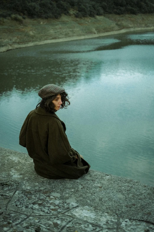 a person sitting by the water, next to the grass