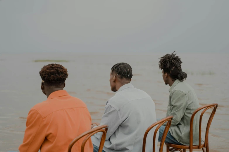 three men sitting at chairs overlooking the water