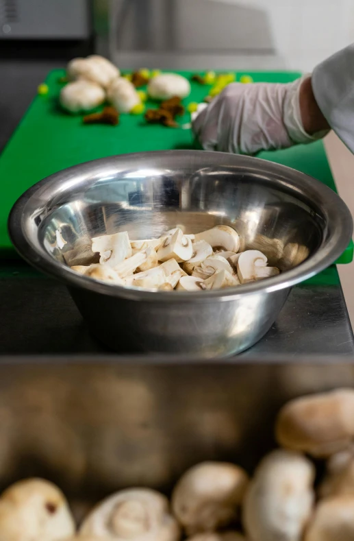 someone wearing gloves in front of a bowl of mushrooms