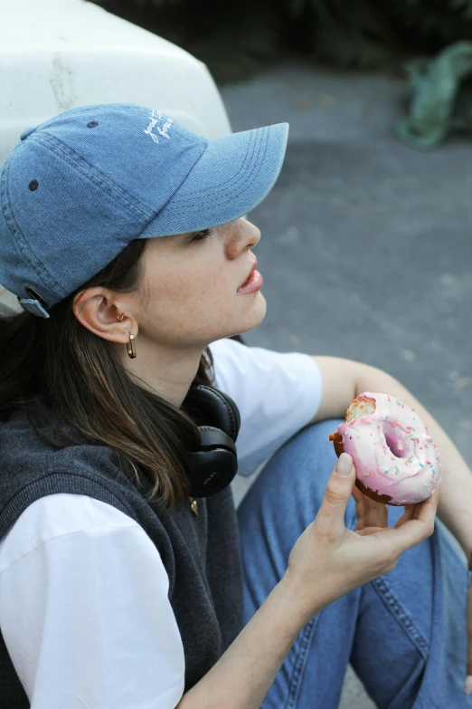 a woman is sitting on the ground eating a pink doughnut