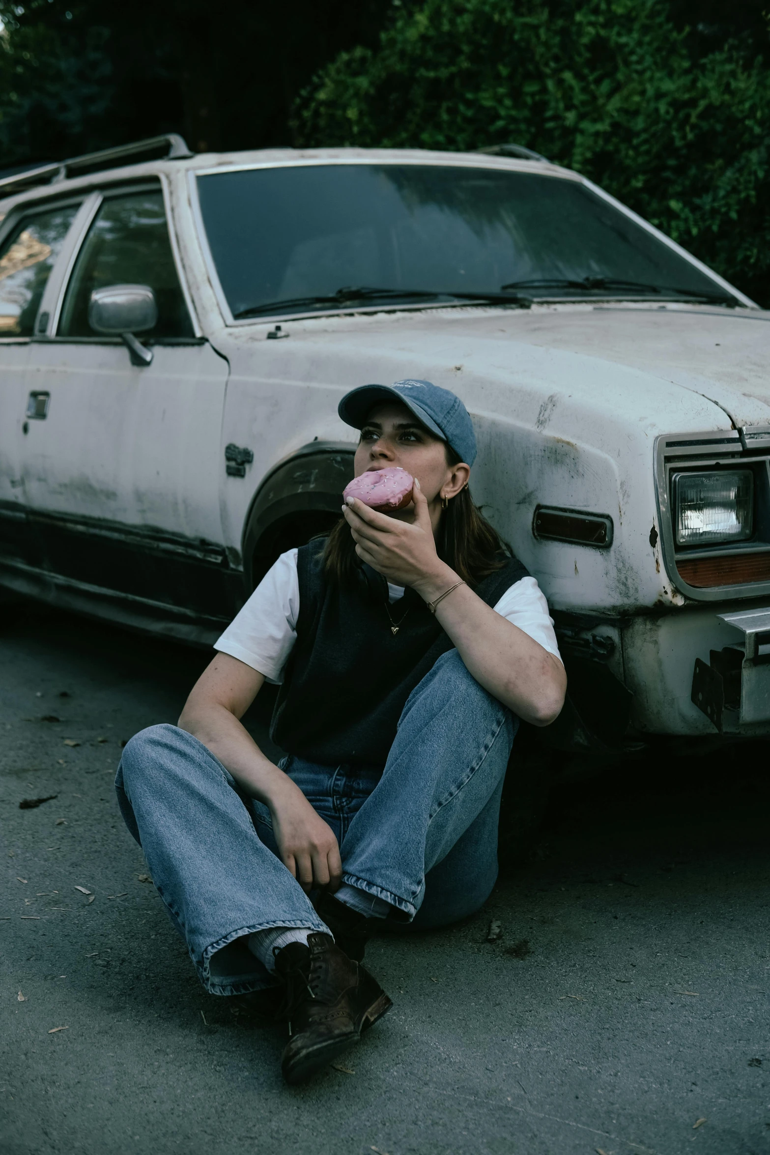 a girl squatting down next to a dirty car eating