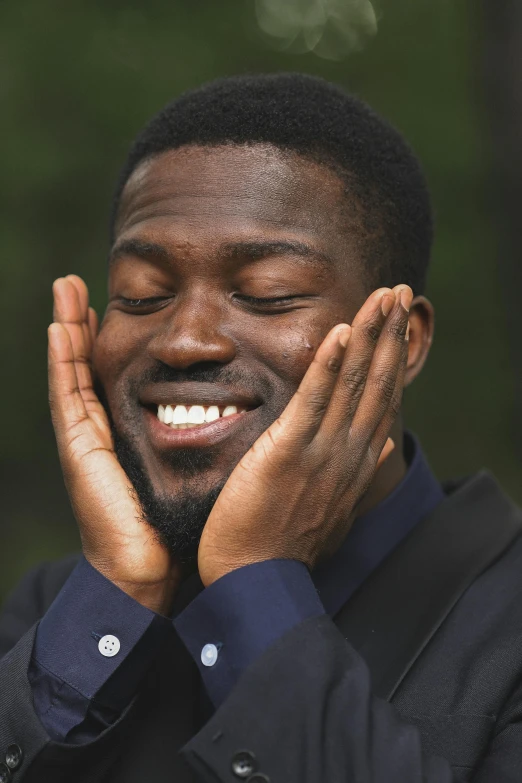 a man smiles while his hands clasped against his face