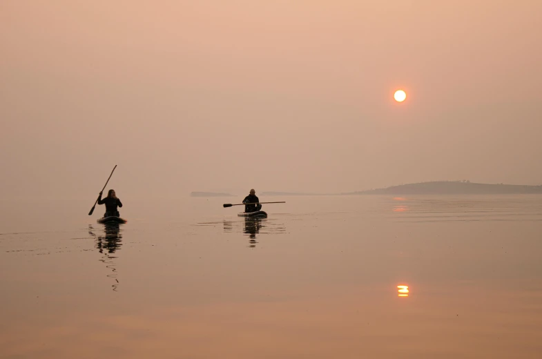 two people ride on their canoes as the sun sets