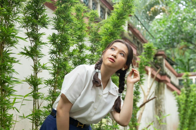 woman in white shirt leaning on bamboo plant with green leaves