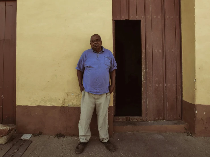 an older man stands outside a building with one arm on his hips