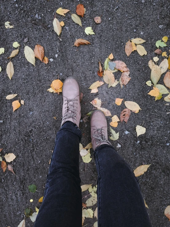 a person standing on a sidewalk with their feet in leaves