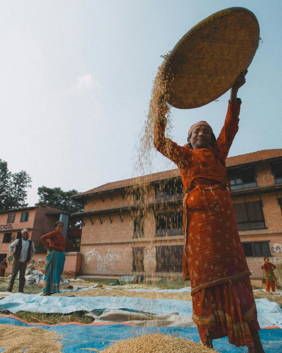 two people throwing corn onto a field and one woman with a large tray on her head