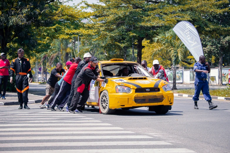 people lined up at the side of a street behind a yellow car