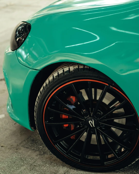 close up of a teal colored car, with an orange stripe on the rear wheel