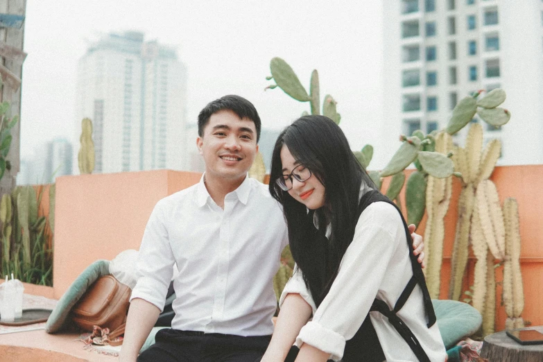 an asian couple poses for a pograph while holding each other in front of cacti