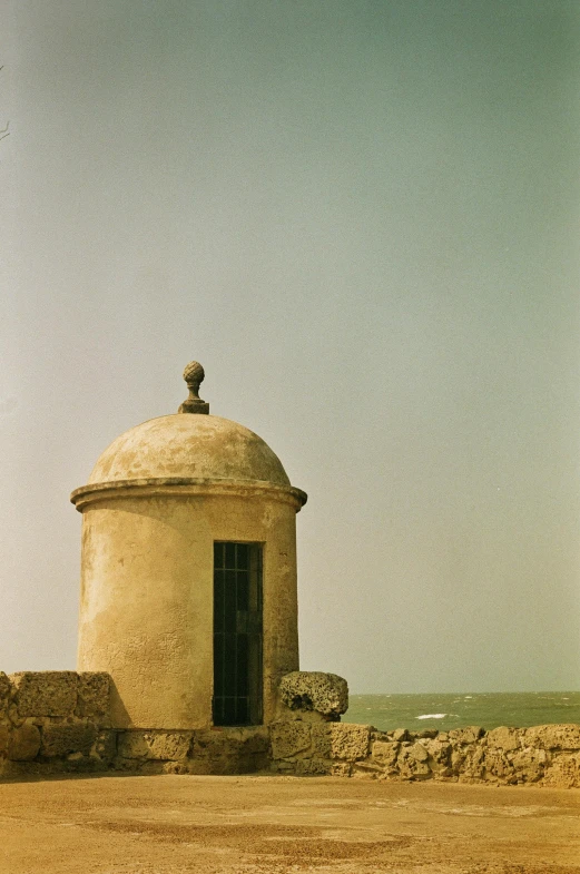 a small white house in the middle of a dirt lot near the ocean