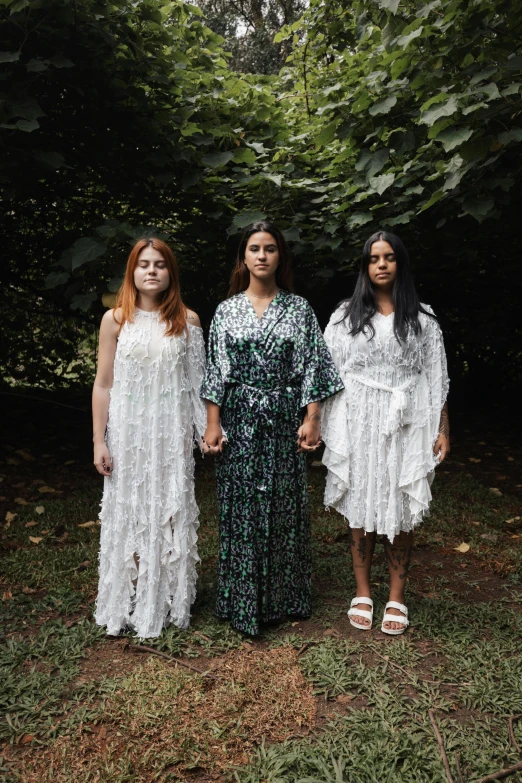 three women in white gowns are standing in a field