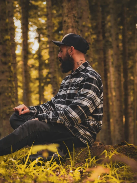 a man in plaid shirt sitting in grass next to trees